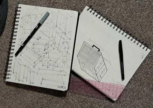 an image of pens, a ruler, and my notebooks with some practice drawings and a three dimensional house